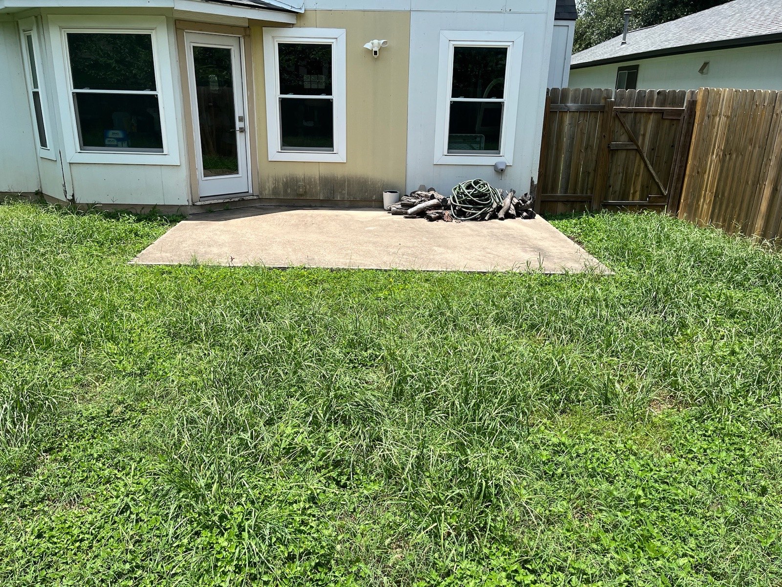Overgrown backyard with a bare concrete slab before the patio and pergola build